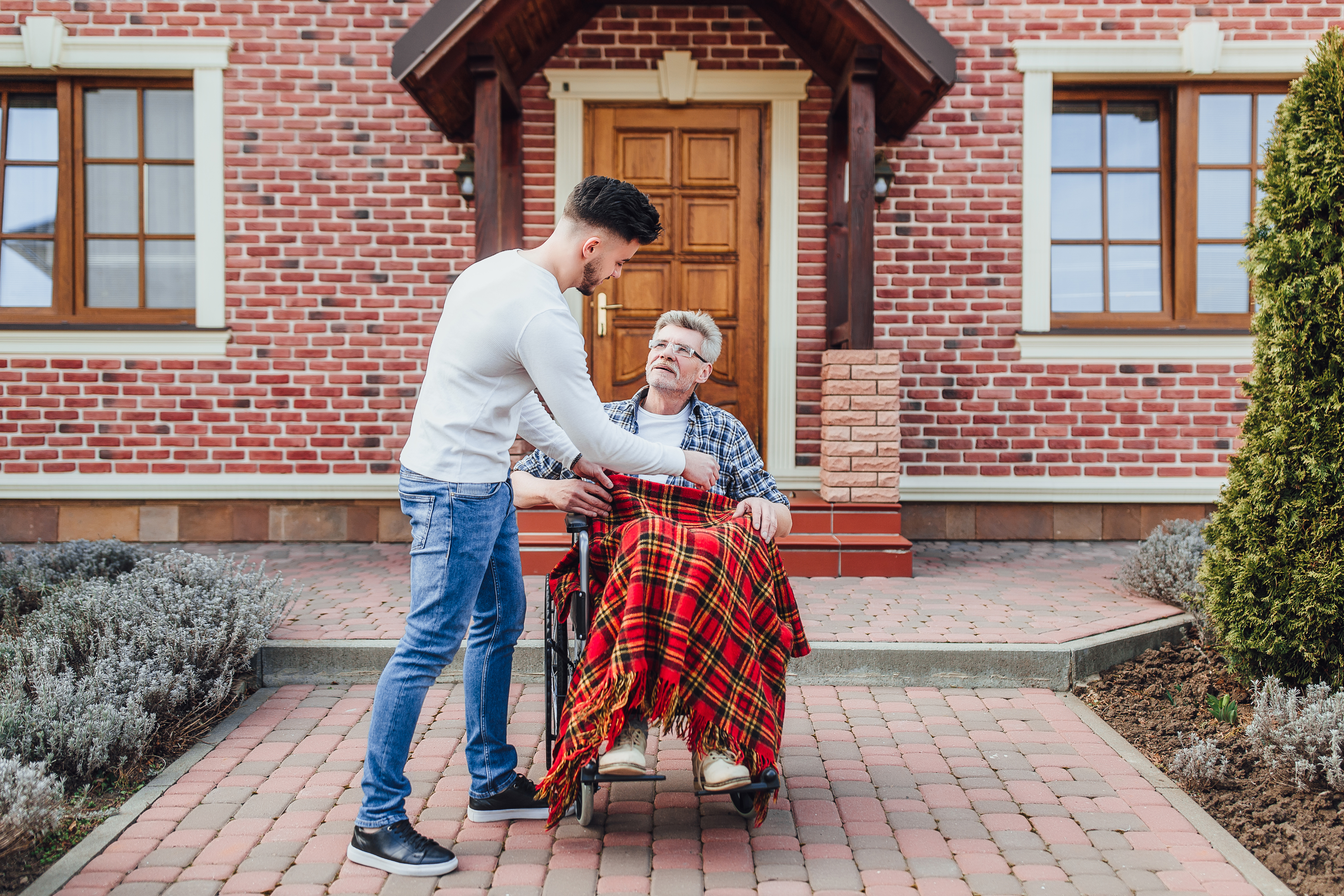 Adult son helping his father in a wheelchair outside a nursing home