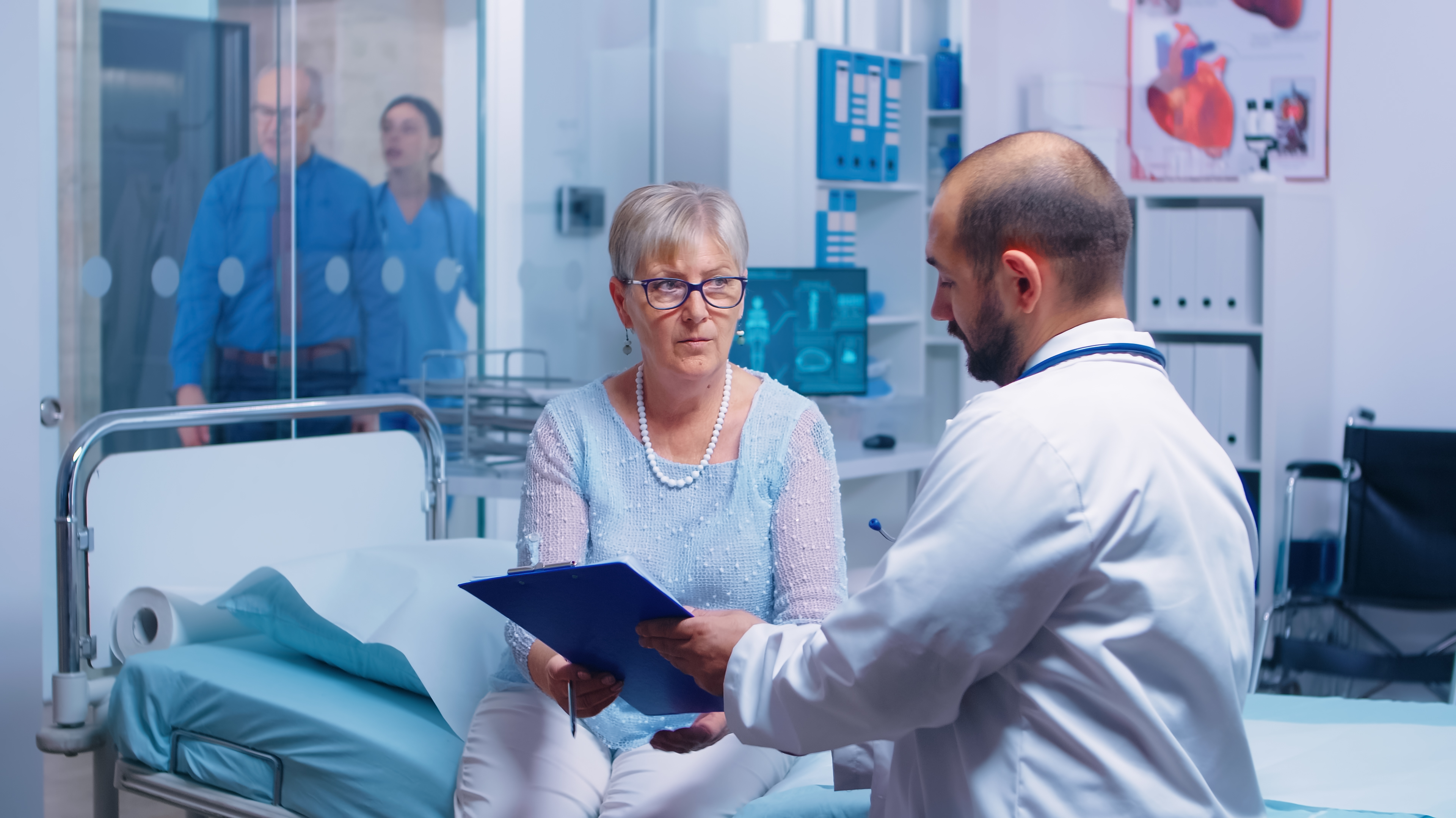 Older patient reviewing paperwork with a clinician at a hospital bedside